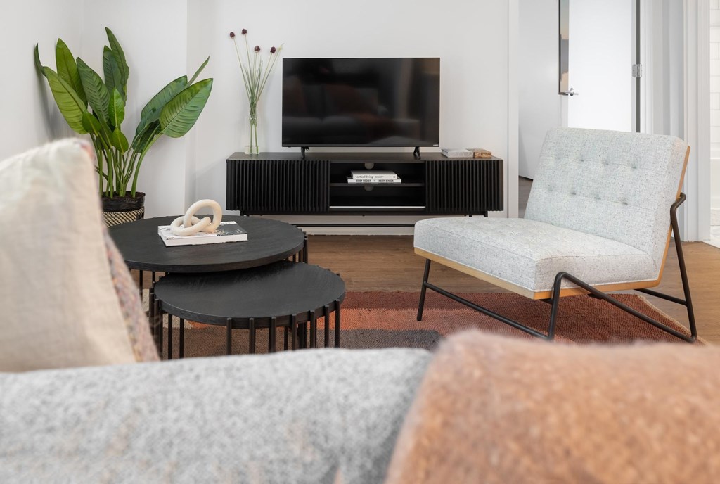 A living room with a grey chair, a black table, and a television.