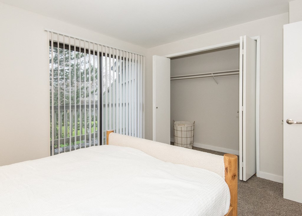 a bedroom with a large white bed and a large window with vertical blinds