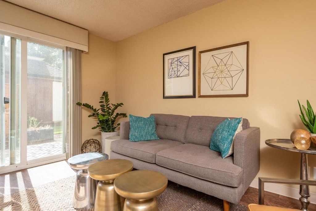 A grey couch with a blue pillow is in the middle of a room with two tables and two framed pictures on the wall.
