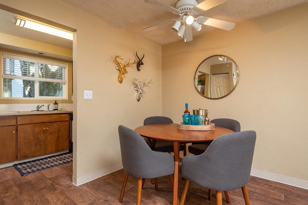 A dining room with a round mirror, a wooden table, and grey chairs.