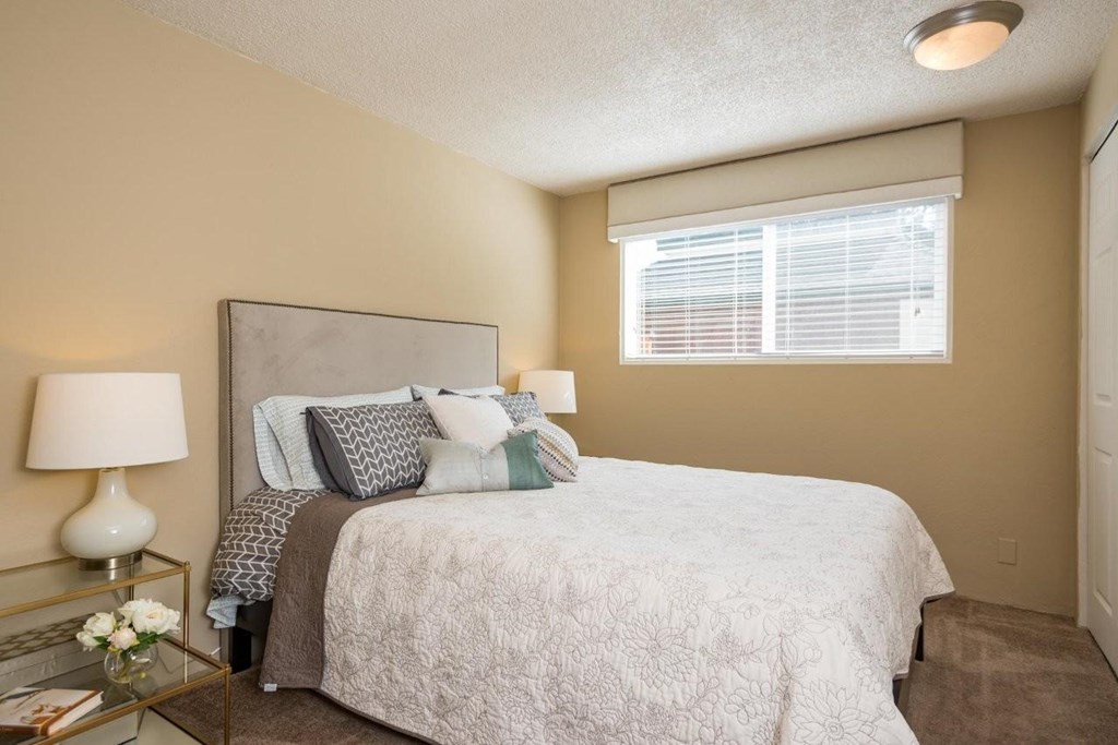 A bedroom with a bed, nightstand, and window.