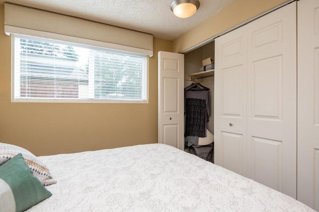 A bedroom with a bed, a window with blinds, and a closet.