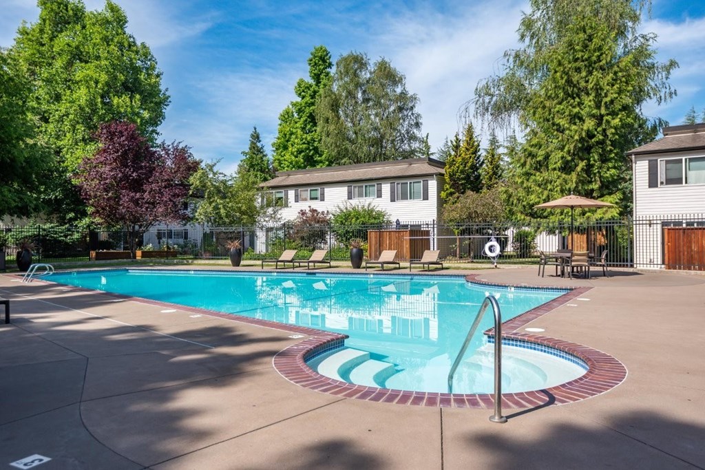 A large outdoor swimming pool surrounded by trees and a white building.