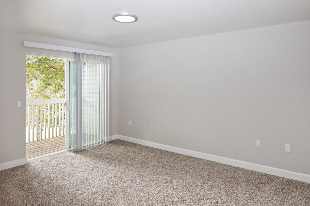 A room with a carpeted floor and a sliding glass door leading to a deck.
