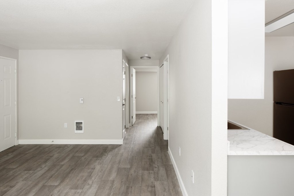 A long, empty hallway with wood flooring and white walls.