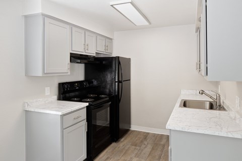 A black refrigerator sits in a kitchen with white cabinets and a marble countertop.