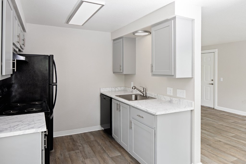 A kitchen with a black fridge, white cabinets, and a marble countertop.
