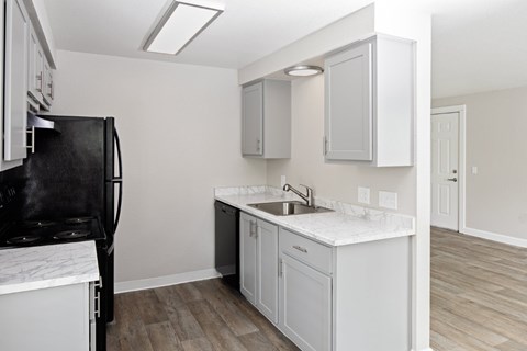 A kitchen with a black fridge, white cabinets, and a marble countertop.