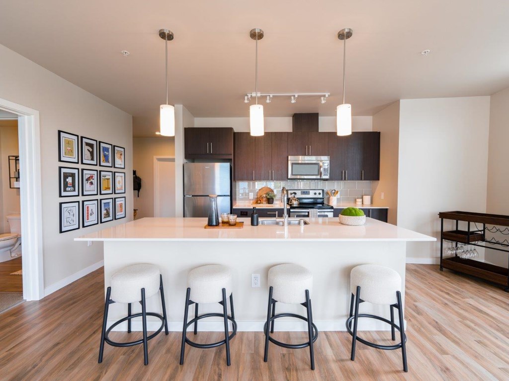A modern kitchen with a white island and black chairs.