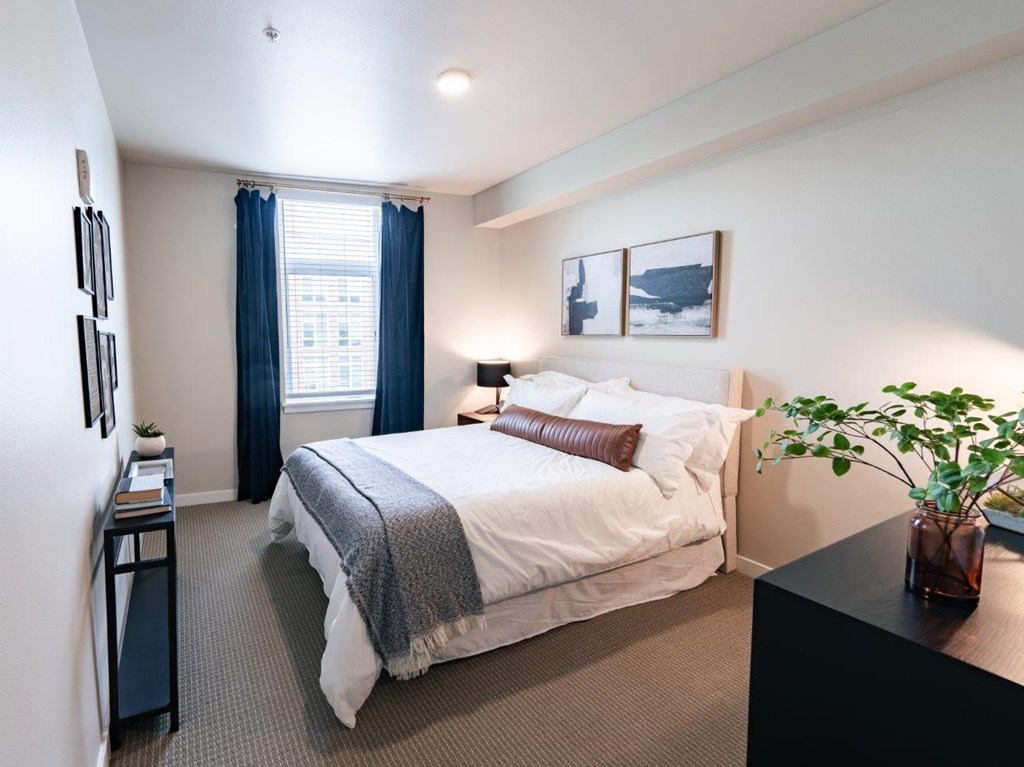 A bedroom with a bed, nightstand, and a plant.