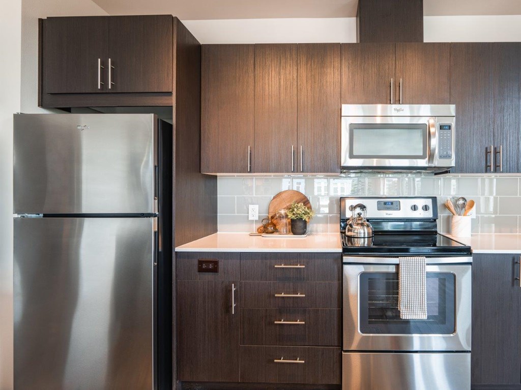 A modern kitchen with a stainless steel refrigerator, microwave, and oven.