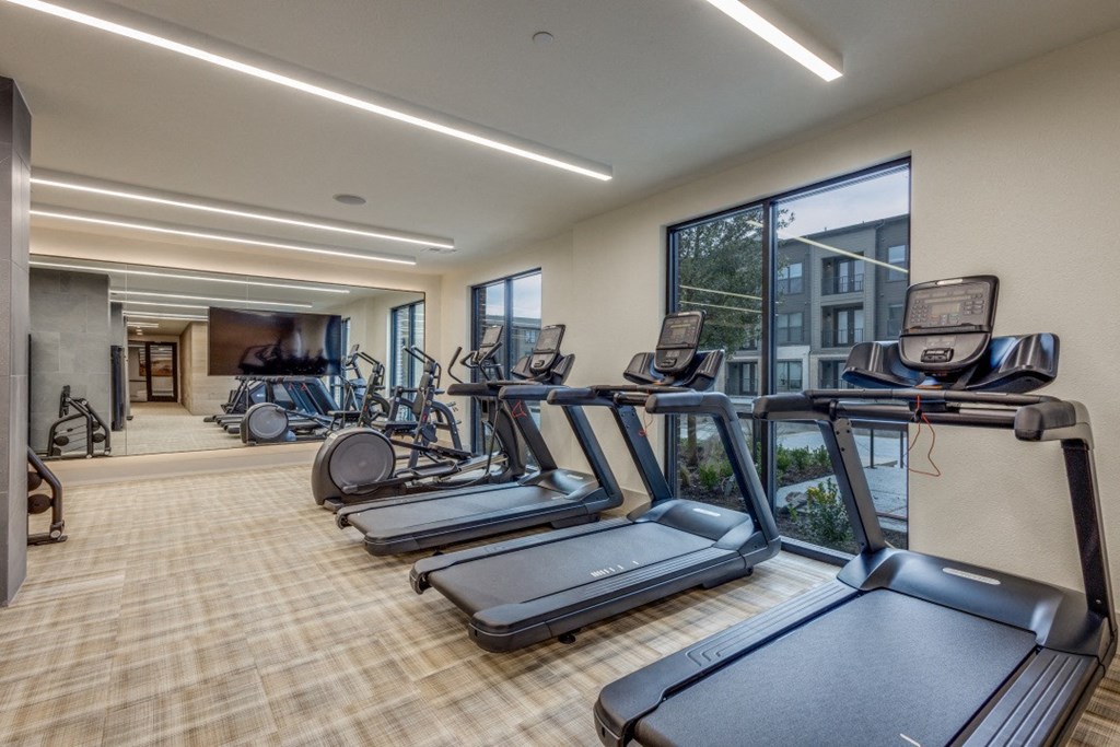 a gym with cardio equipment and a large window