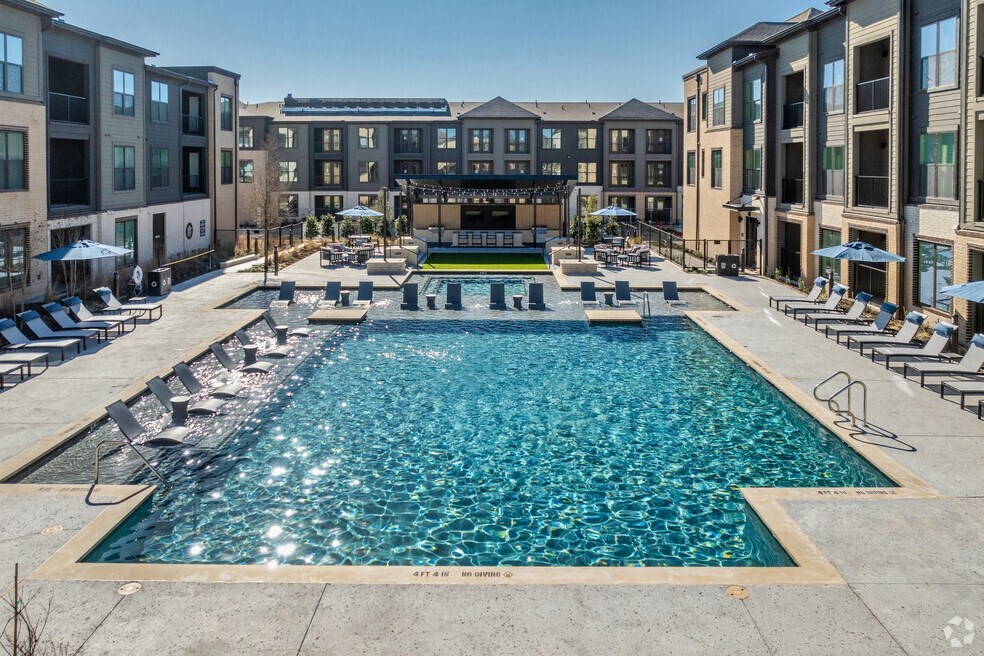 a large swimming pool with lounge chairs in front of an apartment building