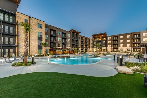 A swimming pool surrounded by a grassy area and apartment buildings.