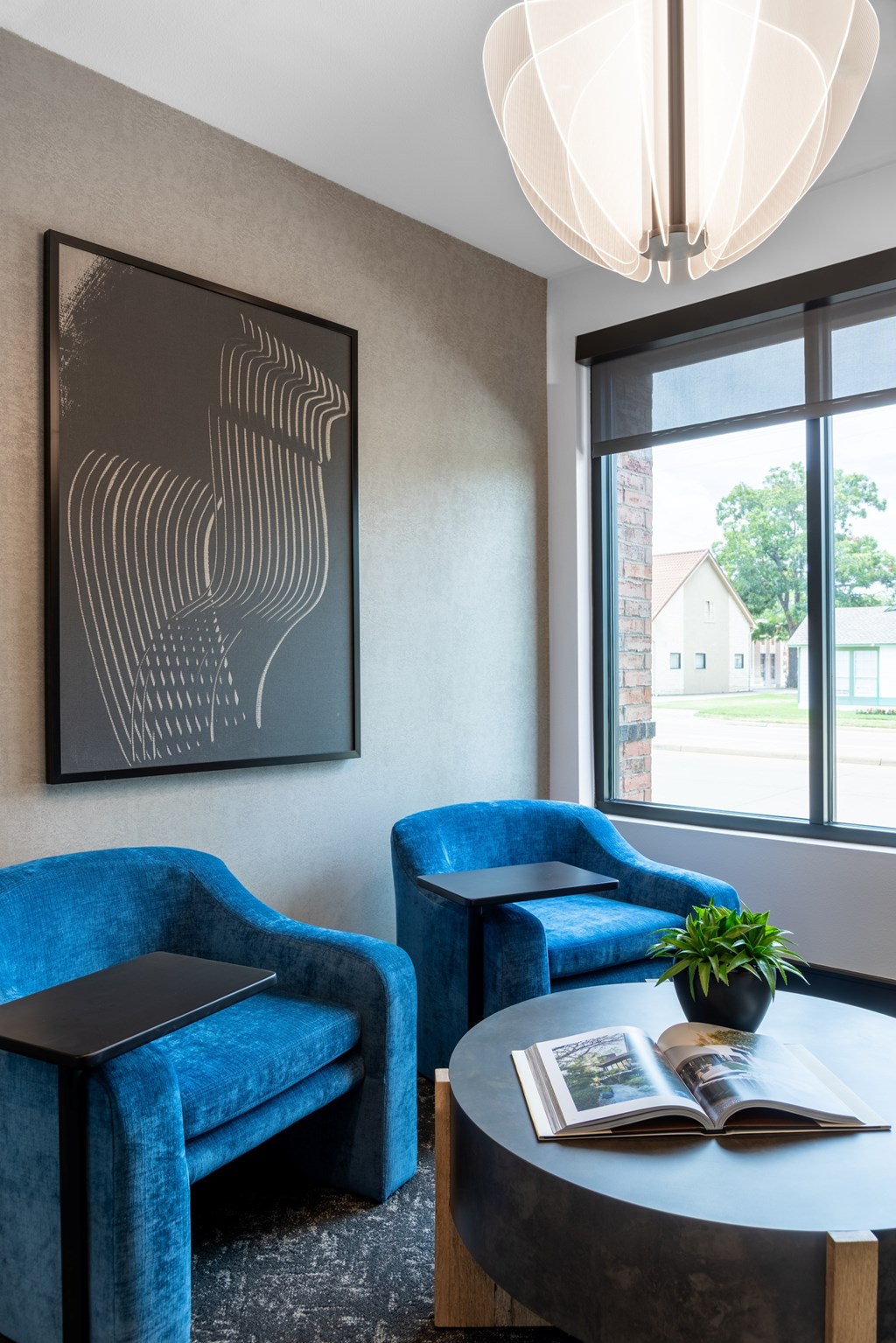 A room with blue chairs, a table with a book and a potted plant on it, and a framed artwork on the wall.