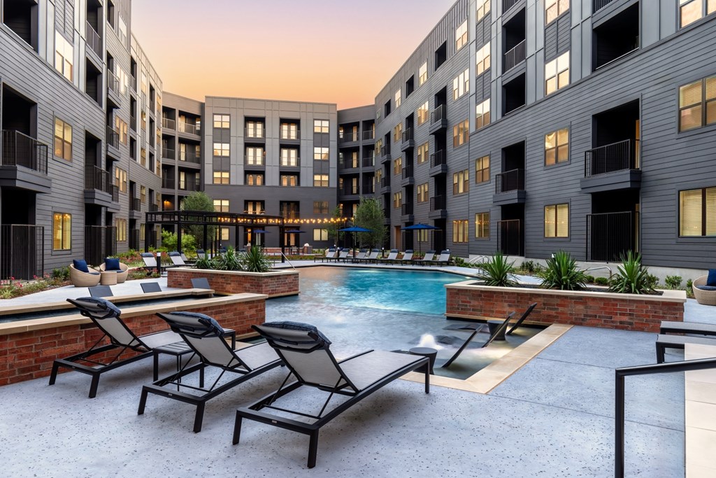 A pool surrounded by lounge chairs in front of apartment buildings.