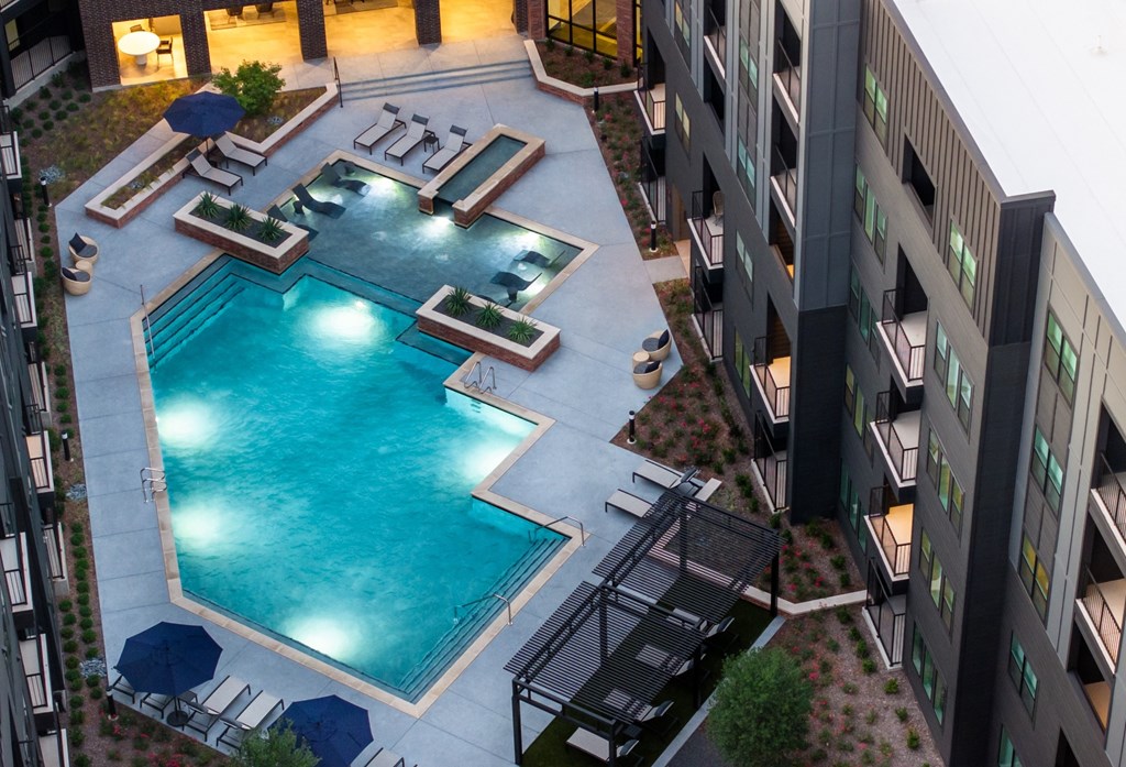 A swimming pool surrounded by a patio area with chairs and umbrellas.
