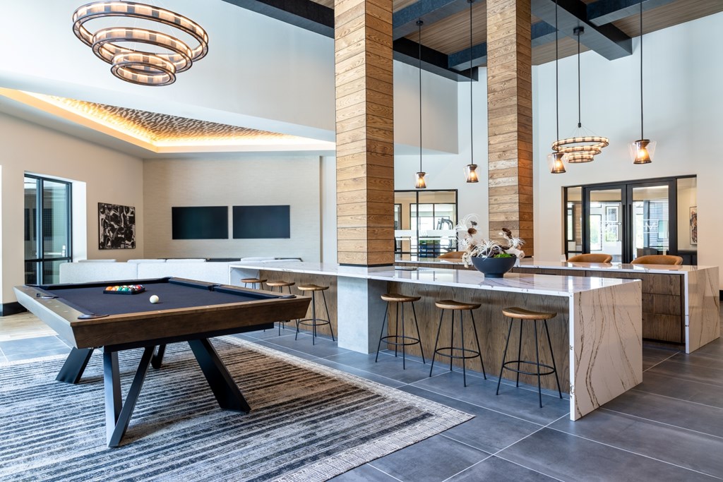 A pool table is in the middle of a room with a bar.