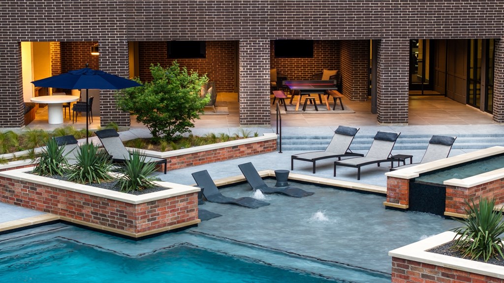 A pool surrounded by a brick wall with a table and chairs.