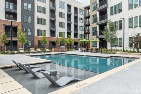 A swimming pool surrounded by modern buildings and lounge chairs.