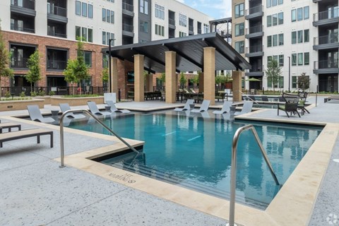 A pool surrounded by chairs and a building in the background.