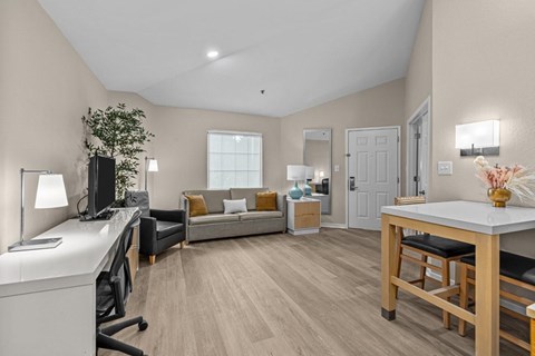 A well-lit room with a desk, couch, and a dining table.