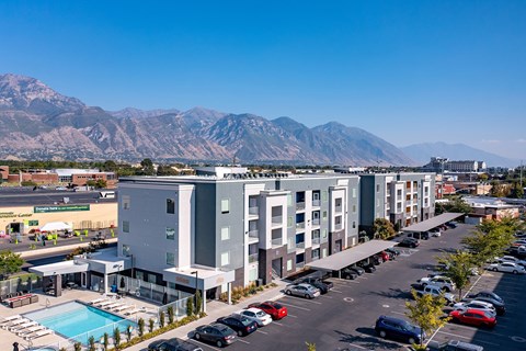 A parking lot with cars and a building with a pool in front of a mountain.