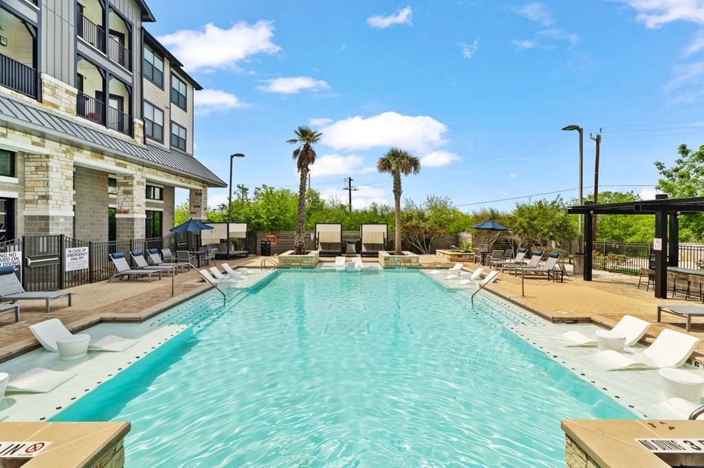 A large swimming pool with lounge chairs and palm trees in the background.