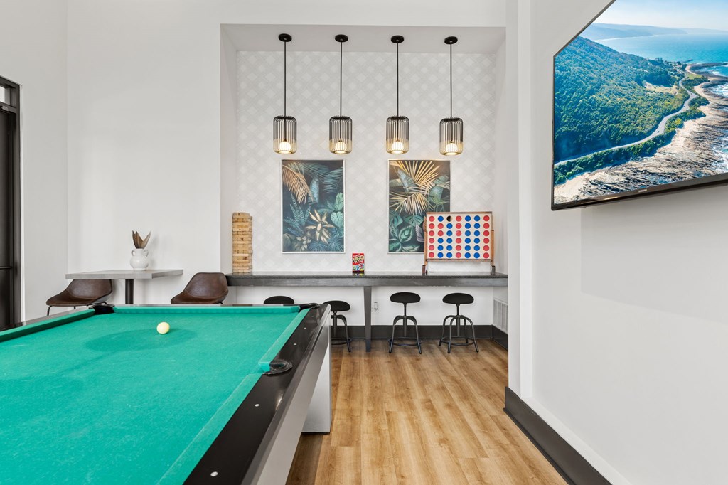 A pool table is in the middle of a room with a bar and a picture on the wall.