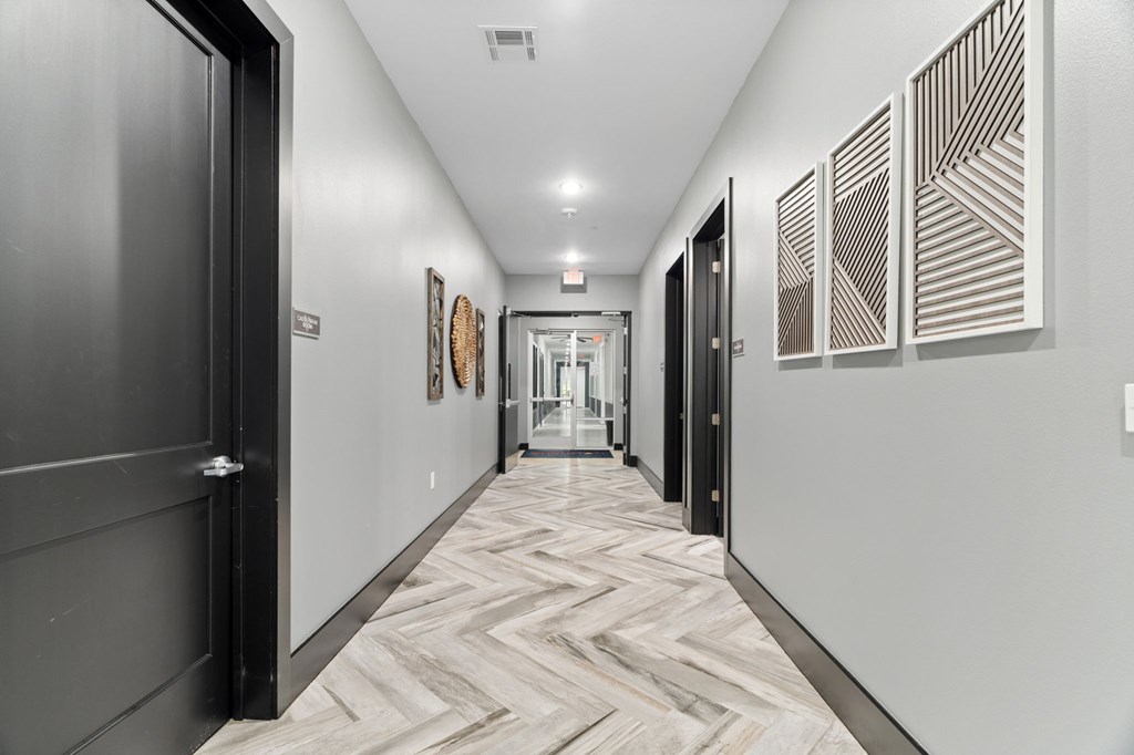 A long hallway with a black door on the left and a wooden floor.