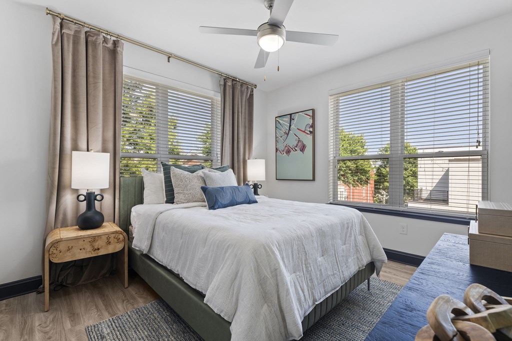A bedroom with a bed, a fan, and a window with blinds.