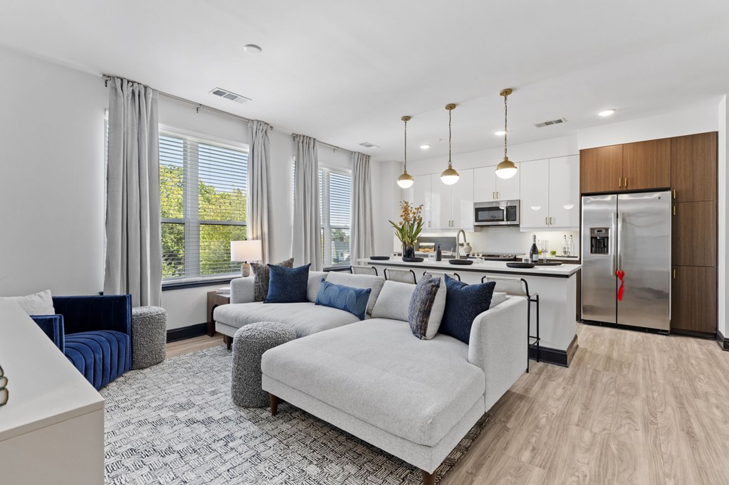 A modern living room with a grey sofa set and a kitchen in the background.