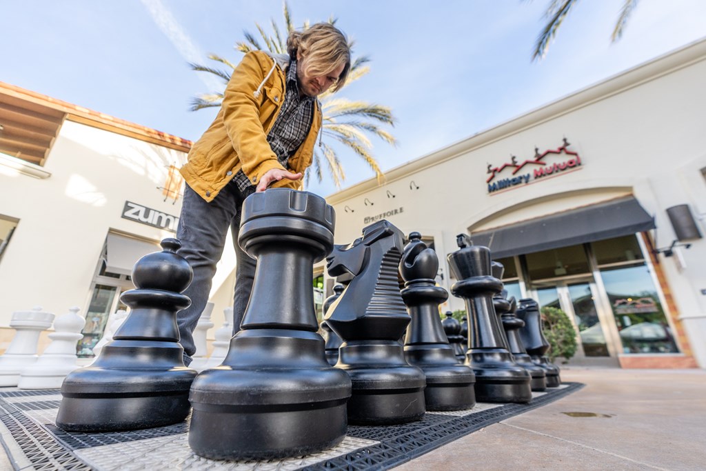A person is playing with giant chess pieces outside a building.