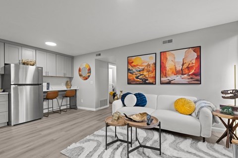 A modern kitchen with a white fridge, a dining table with chairs, a sofa with a yellow pillow, and two paintings on the wall.