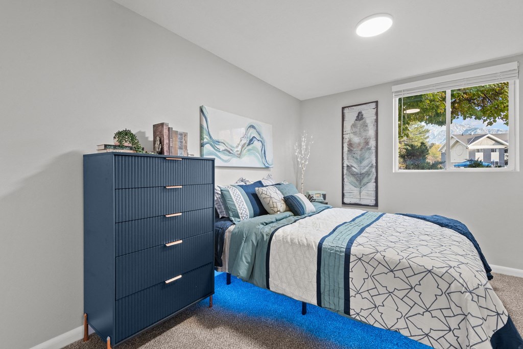 A bedroom with a dark blue dresser and a bed with a blue and white comforter.