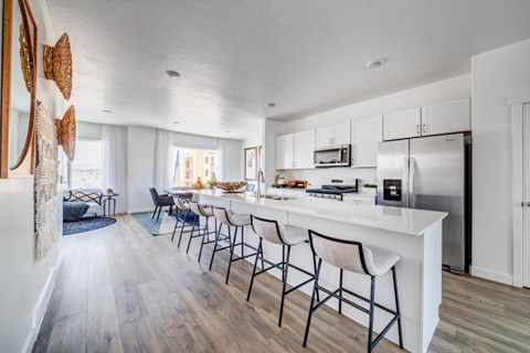 A kitchen with white cabinets and a white island with black chairs.
