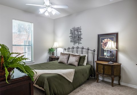 A bedroom with a bed, a ceiling fan, and a painting of a sunflower.