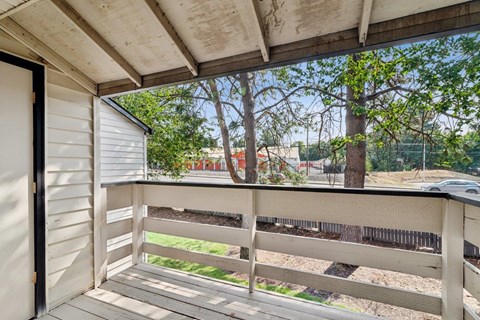 A balcony with a wooden railing and a view of a tree and a fence.