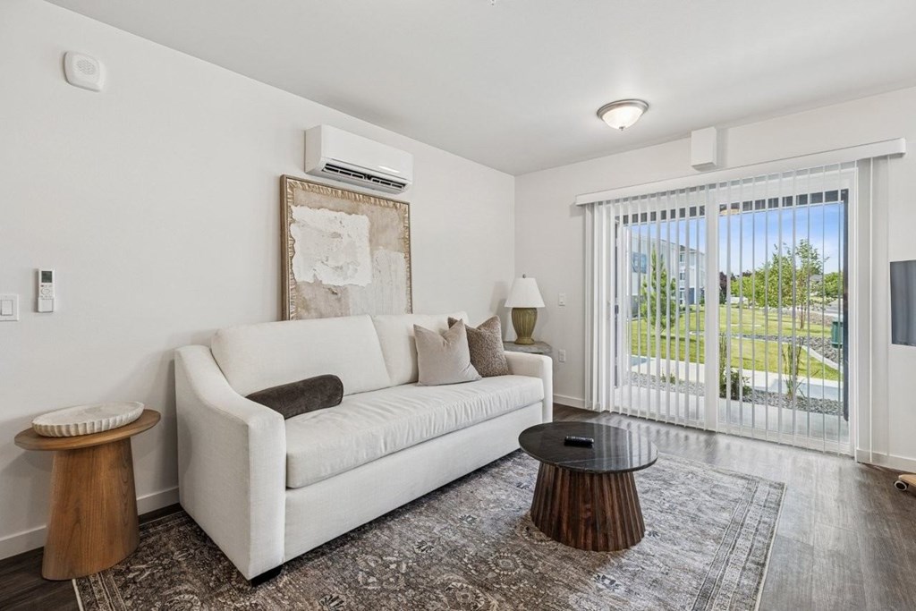 A white couch with a brown pillow is in the middle of a room with a window.