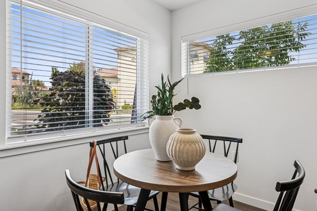 A table with a vase and a plant on it in front of a window.