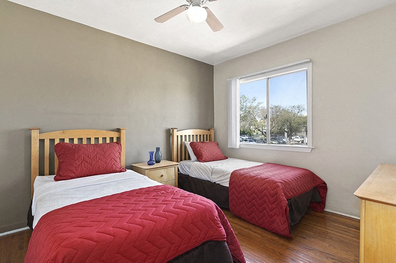 two twin beds in a room with a ceiling fan and a window