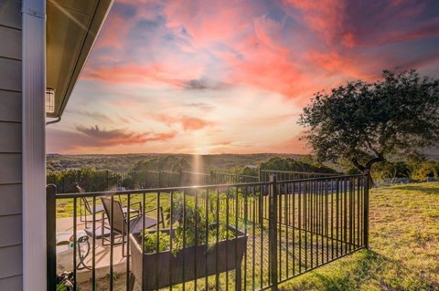 A sunset view from a balcony with a table and chairs.