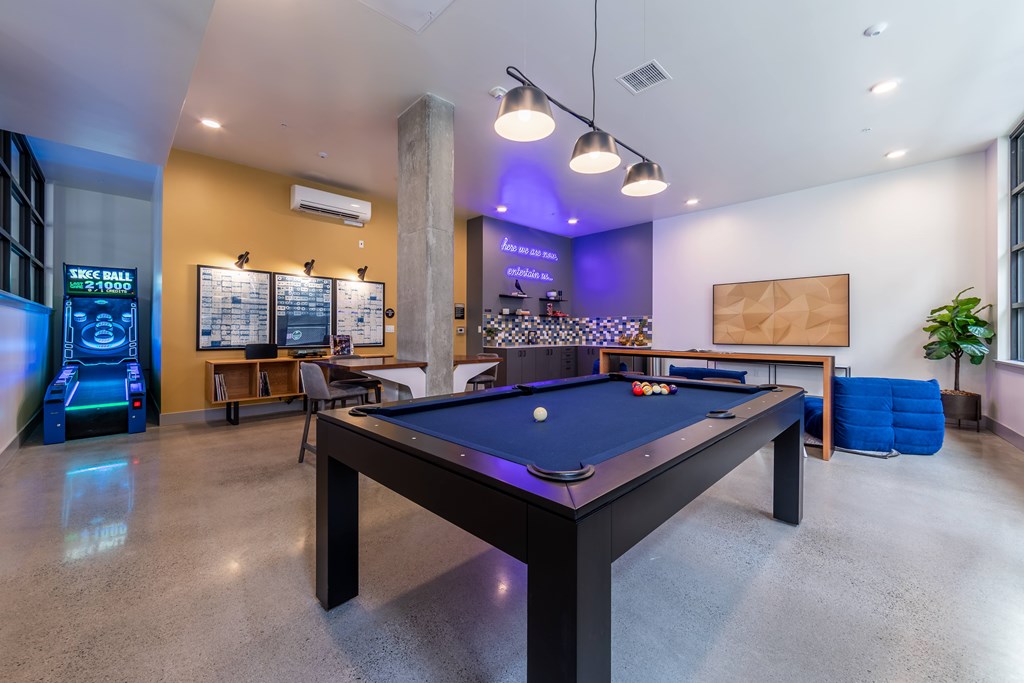 A pool table is in the middle of a room with a foosball table to the left and a shuffleboard table in the background.