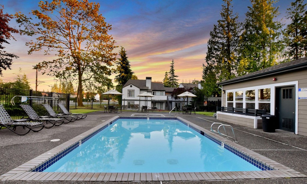 a swimming pool with chairs and a house with a sunset in the background