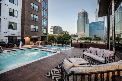 a pool and lounge area on a balcony with a city in the background