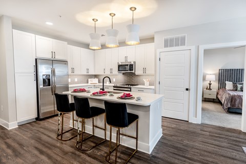 a kitchen with white cabinets and a white island with three black chairs