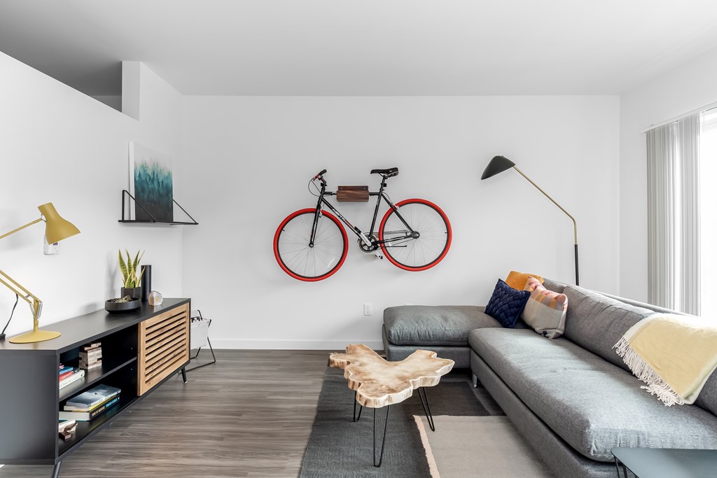 A living room with a grey couch, a bicycle on the wall, and a wooden floor.