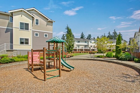 A playground with a green slide and a red swing set in front of apartment buildings.