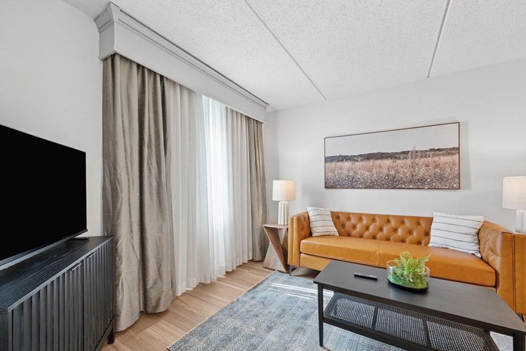 A living room with a brown sofa, a black coffee table, a flat screen TV, and a painting on the wall.
