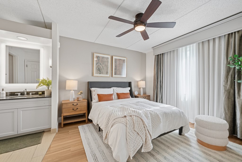 A bedroom with a bed, a ceiling fan, and a nightstand with a lamp.